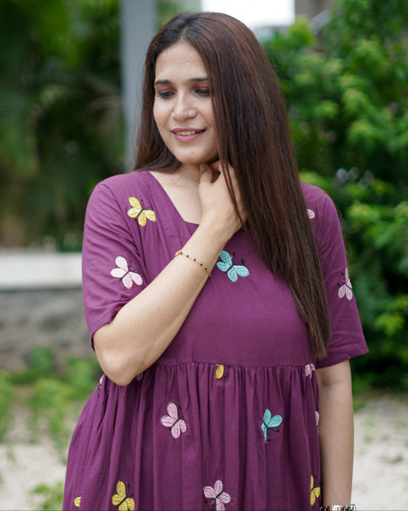 Woman wearing a purple dress with colorful butterfly patterns outdoors.