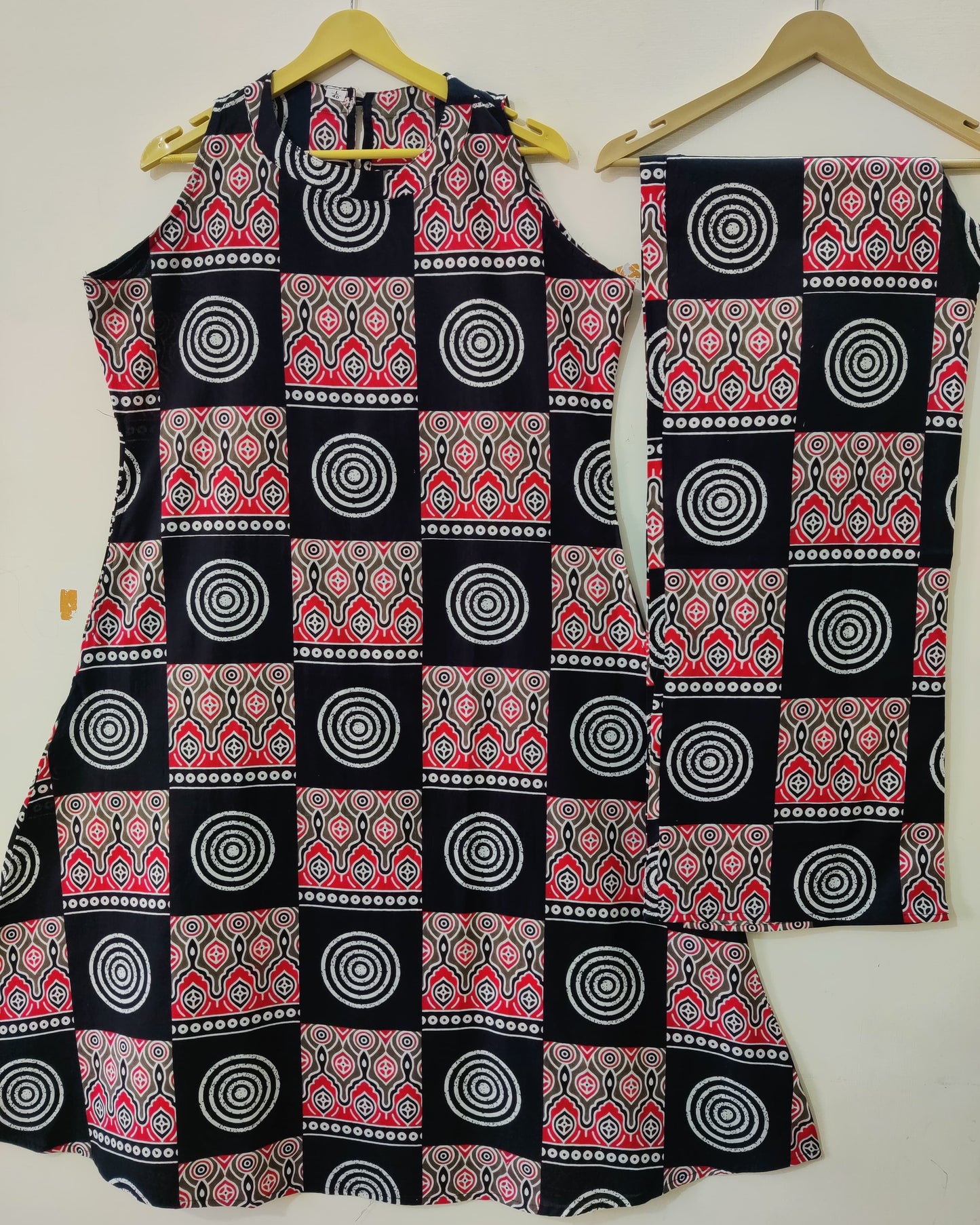 Black sleeveless top and red and white patterned pants on hangers against a white background