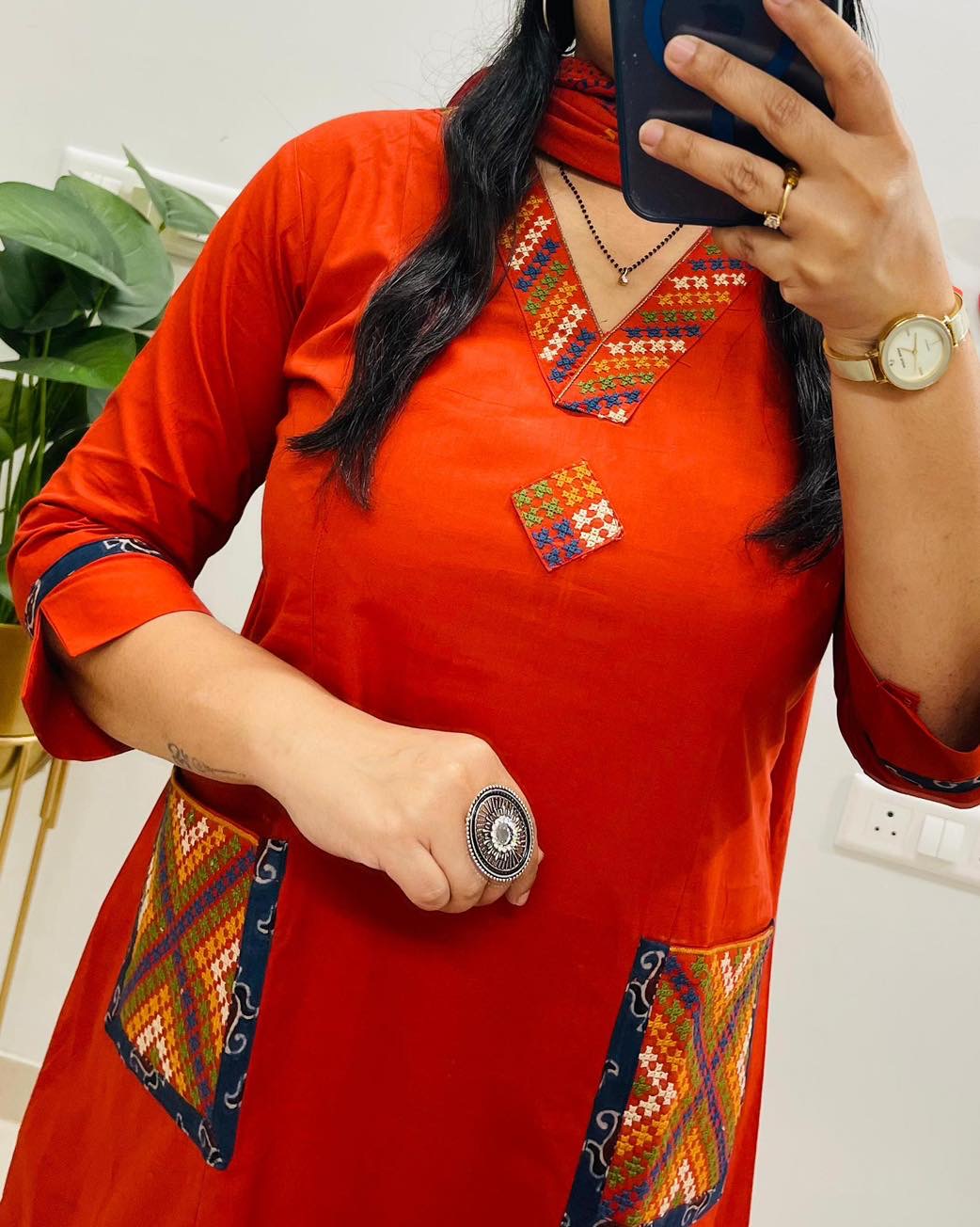 Person wearing a red traditional outfit with intricate patterns, holding a phone.