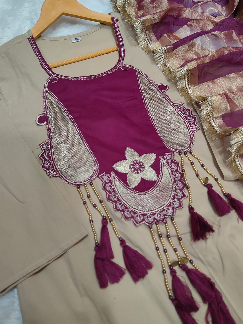 Decorative purple top with intricate embroidery and tassels on a beige background