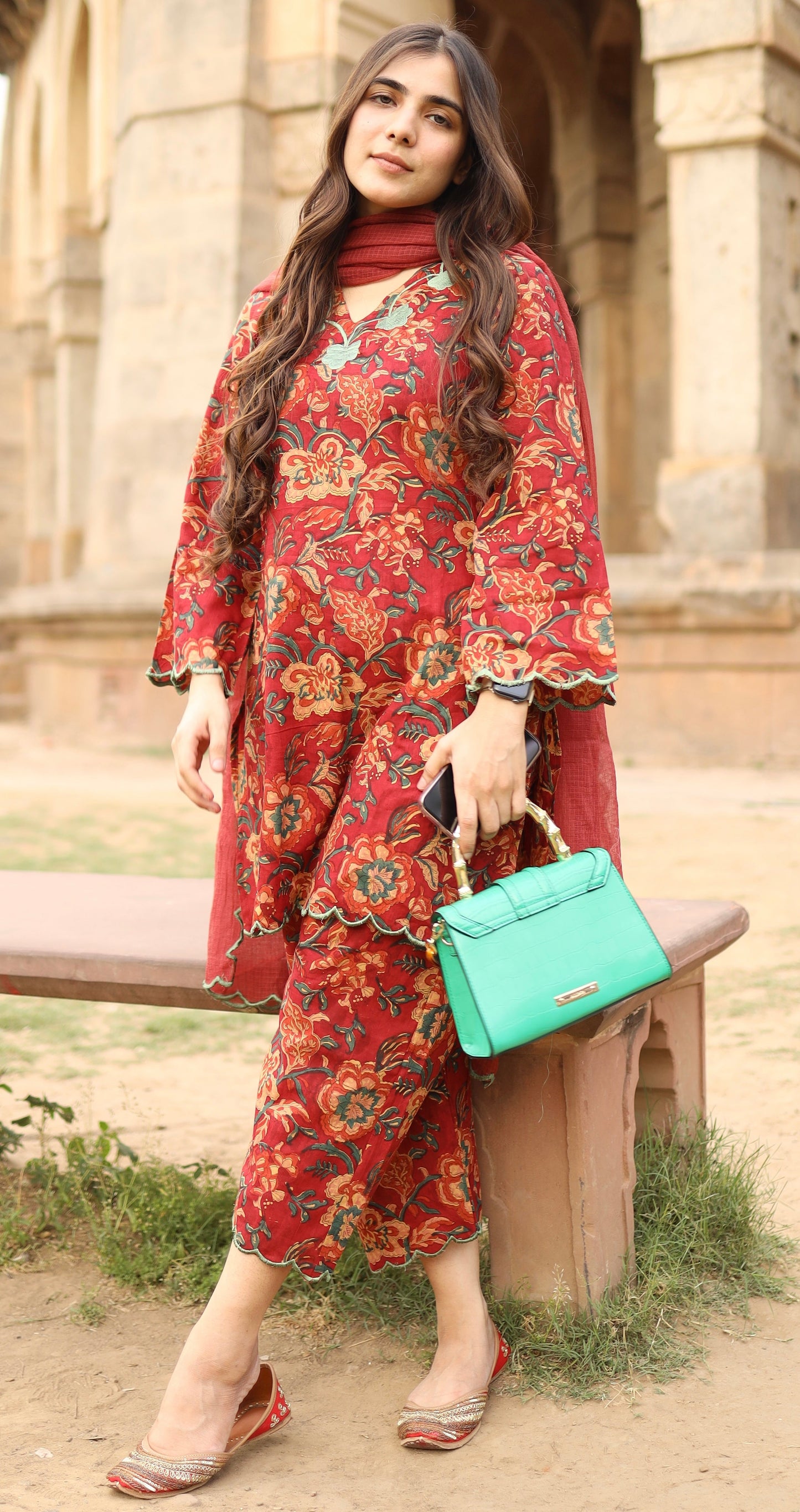 Woman in a red floral dress holding a green handbag outdoors.