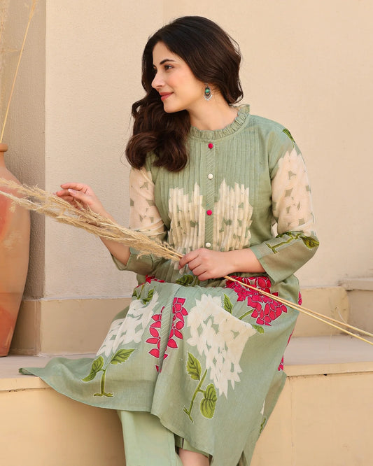Woman wearing a green and white embroidered dress holding a broom.