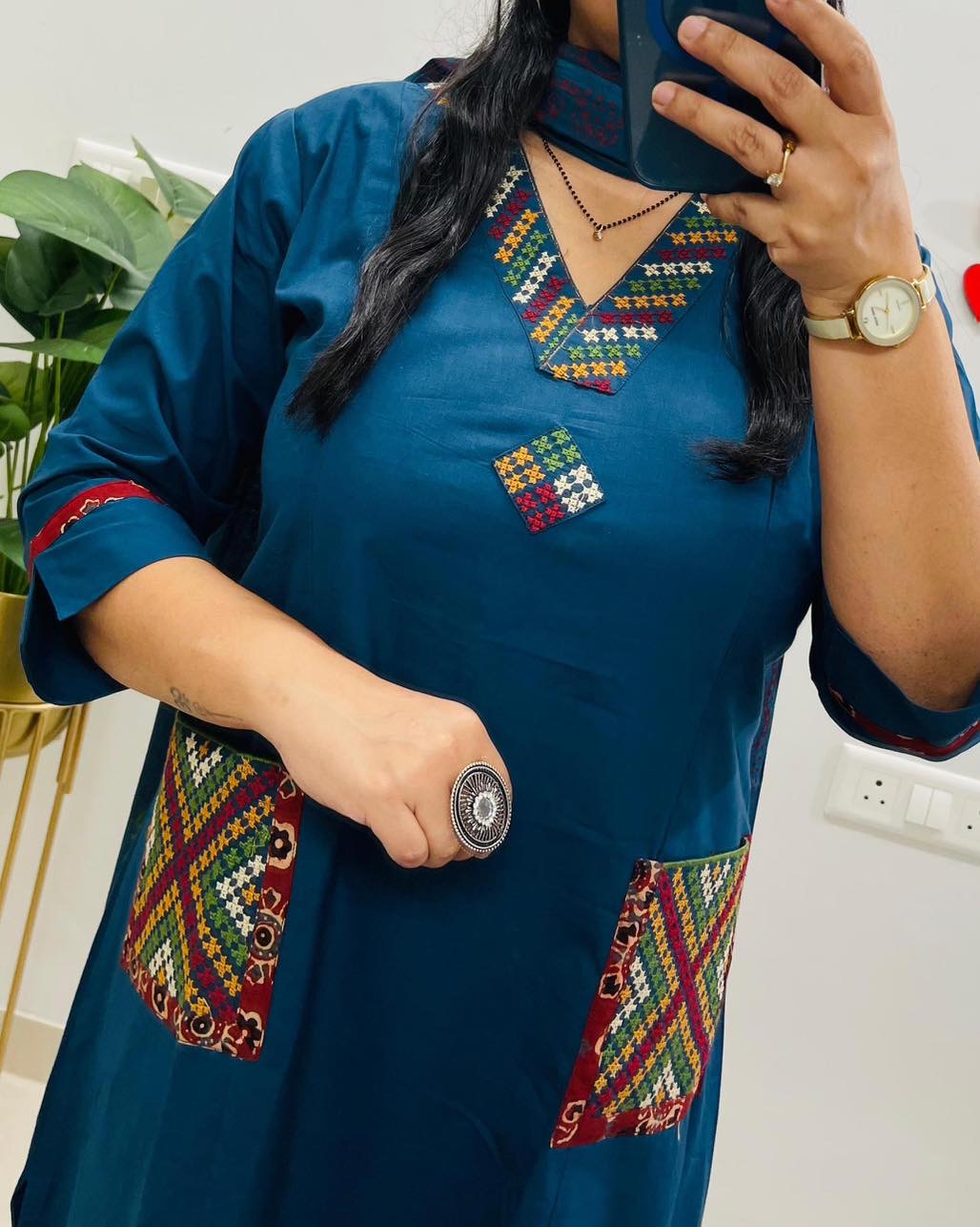 Person wearing a blue dress with colorful embroidery, holding a phone.