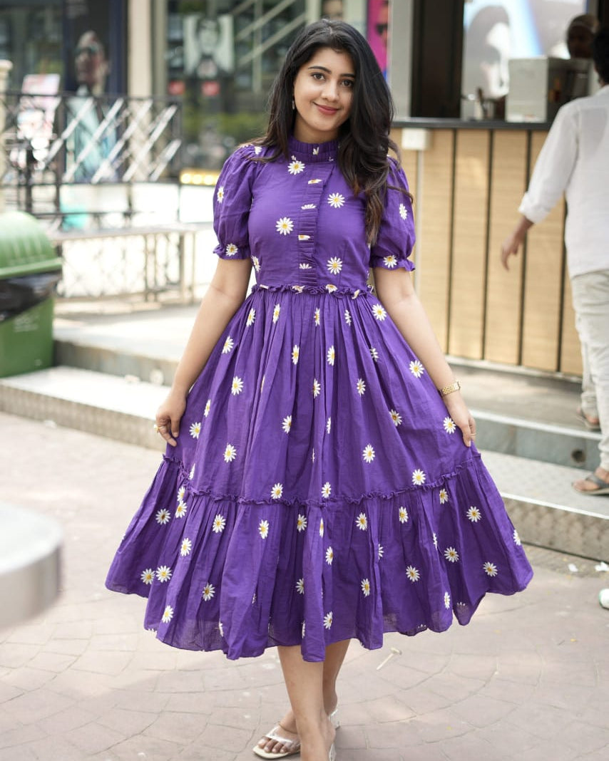 Woman wearing a purple dress with white floral patterns outdoors.