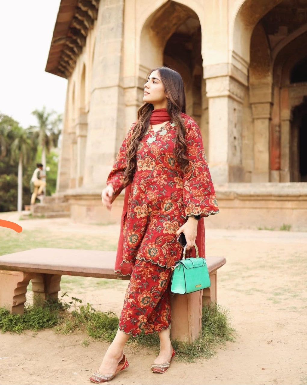 Woman in a red floral outfit standing in front of an architectural structure.
