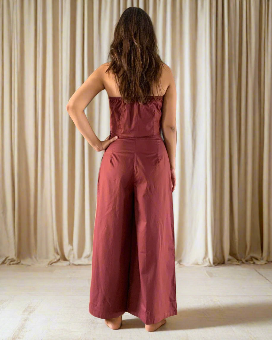 Woman wearing a red jumpsuit standing in a room with wooden flooring and decorative vases.