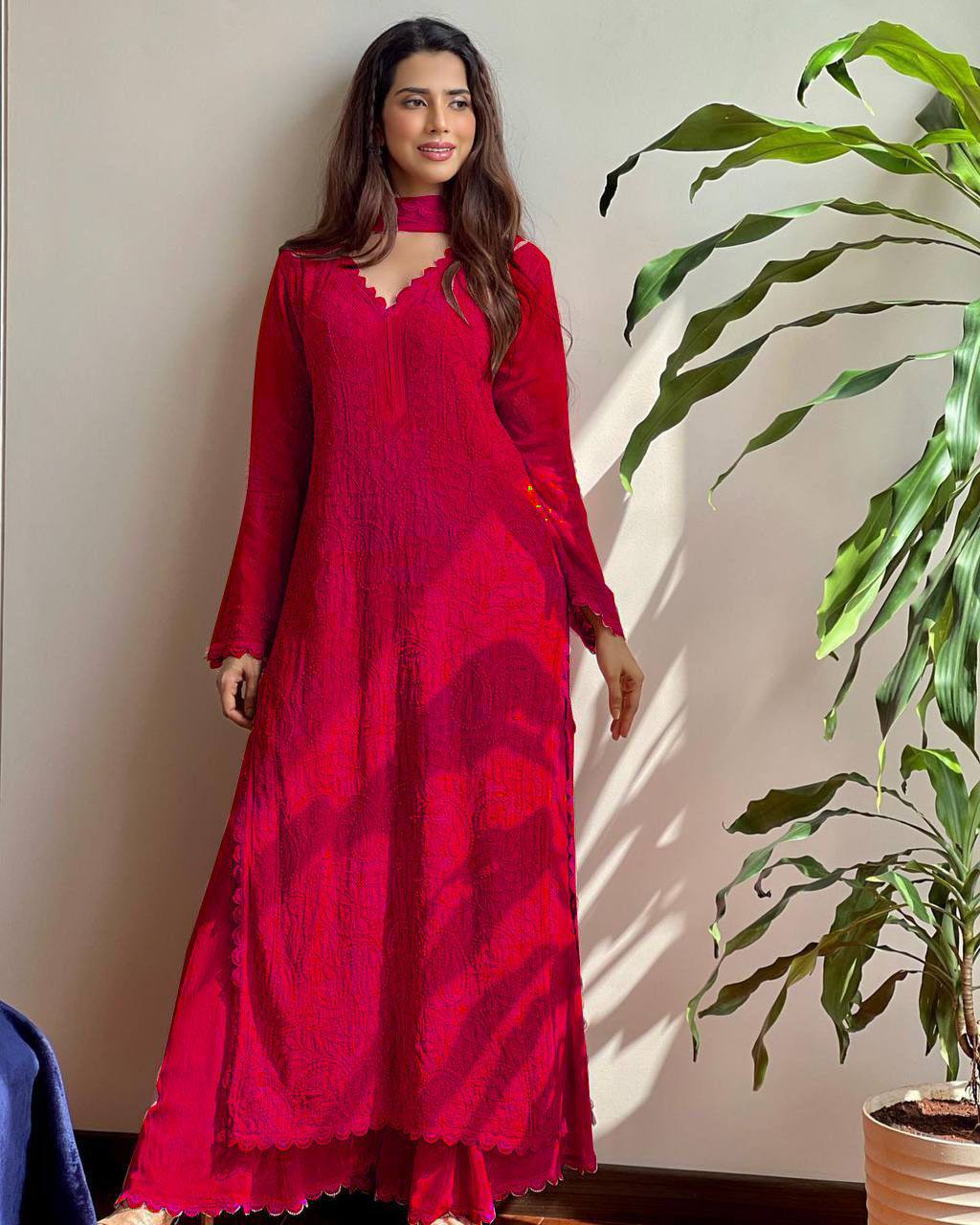 Woman wearing a red dress standing next to a plant indoors