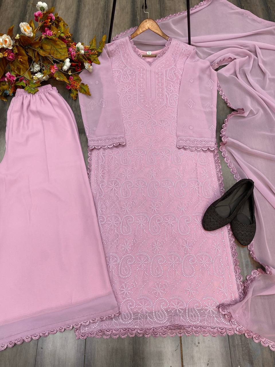 Pink embroidered dress with matching pants and black shoes on a wooden surface.
