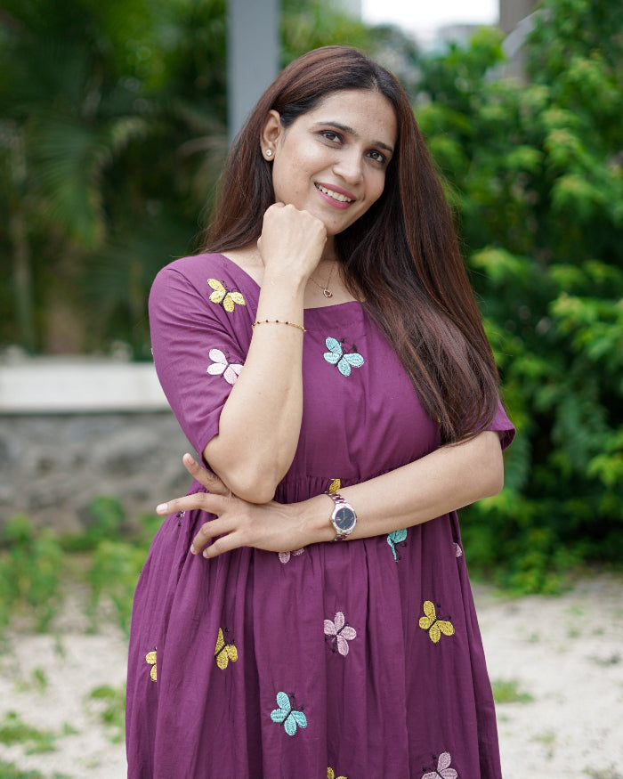 Woman in a purple dress with butterfly patterns standing outdoors.