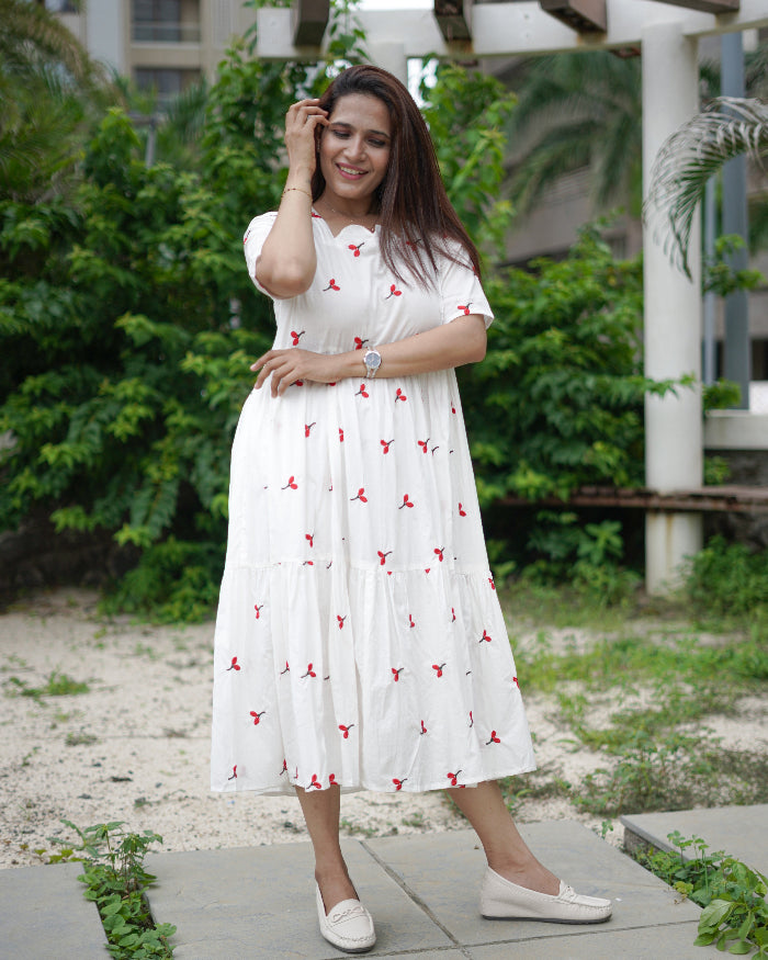 Woman in a white dress with red patterns standing outdoors on a pathway.