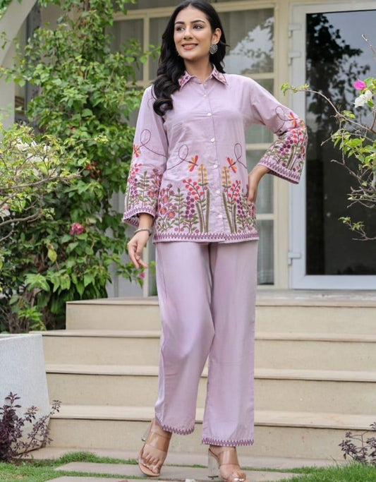 Woman wearing a light pink traditional outfit with floral embroidery outdoors.
