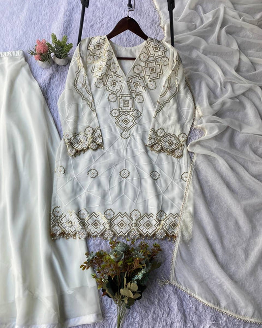 White embroidered outfit with matching pants on a textured surface with flowers.