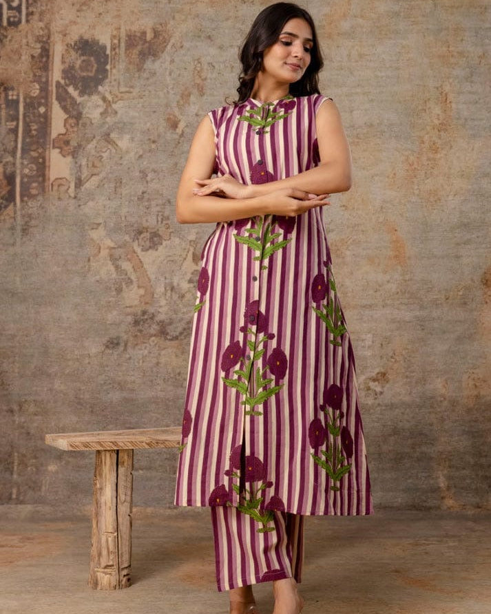 Woman wearing a sleeveless dress with floral pattern against a textured wall.