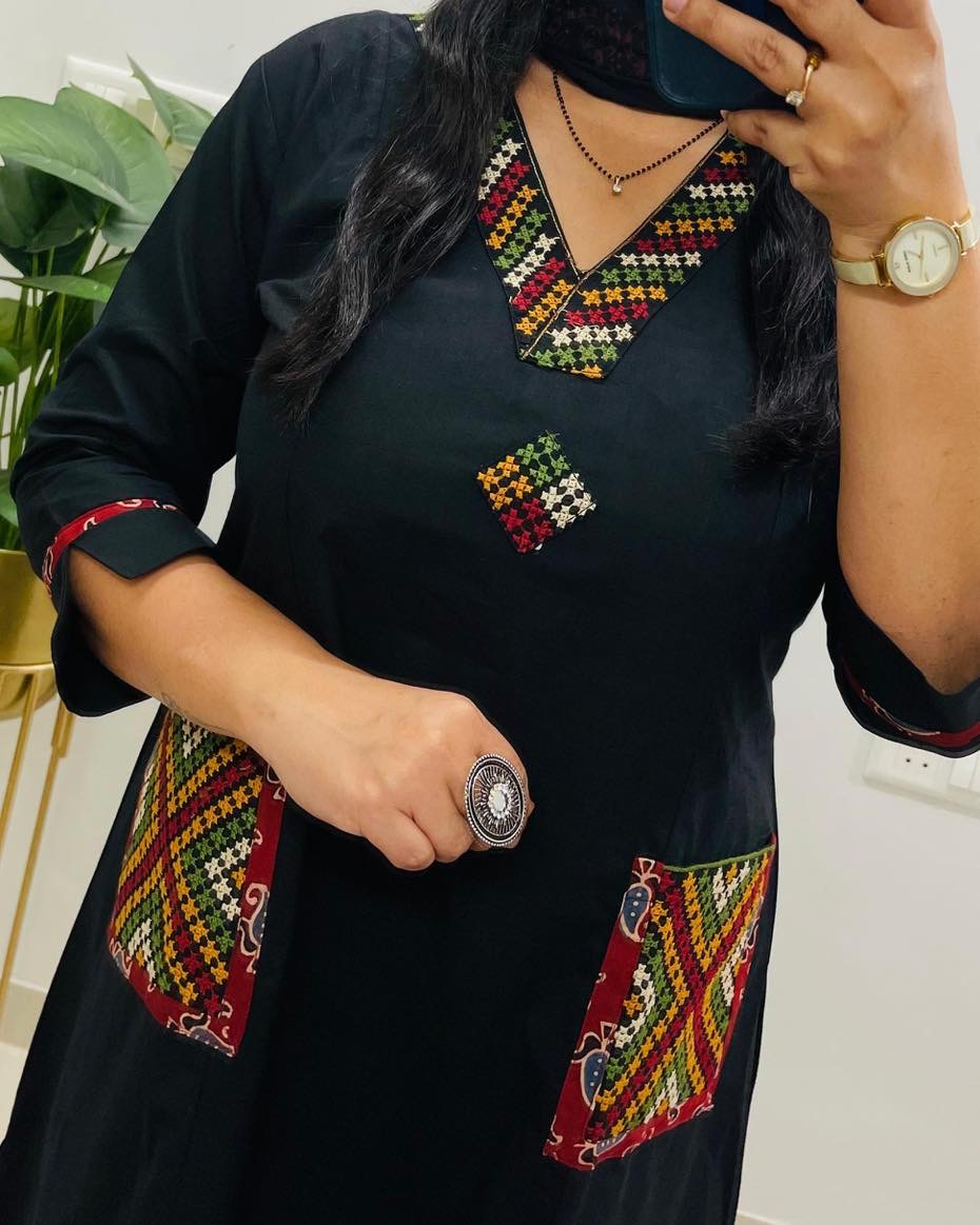 Person wearing a black dress with colorful embroidery, holding a phone.