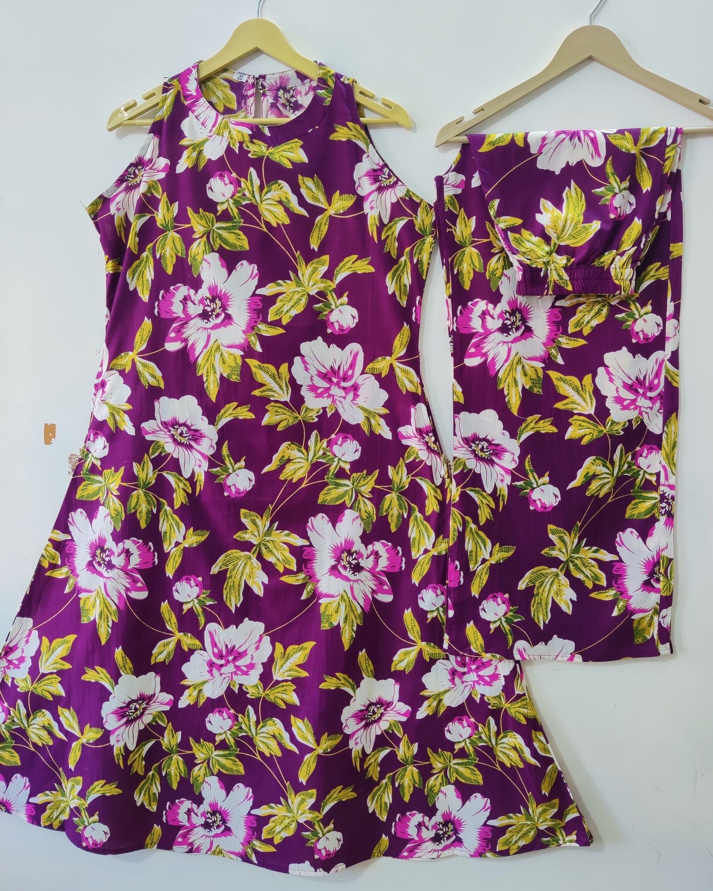 Purple floral dress with matching pants on hangers against a white background