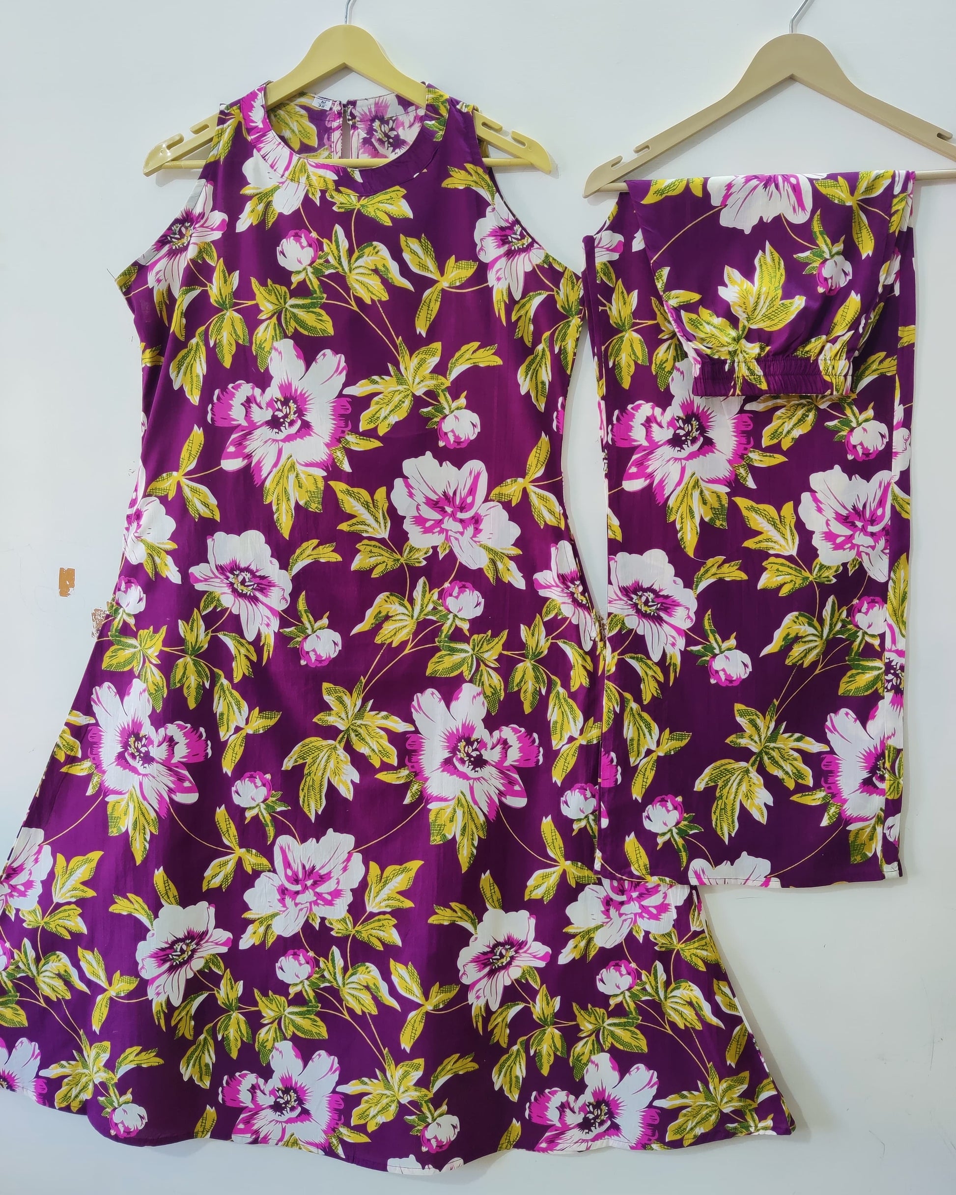 Purple floral dress with matching pants on hangers against a white background