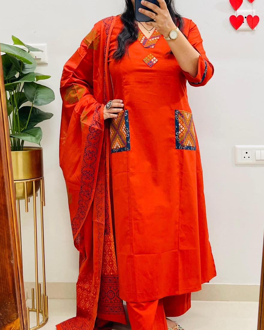Person wearing an orange traditional outfit with patterns, standing indoors.