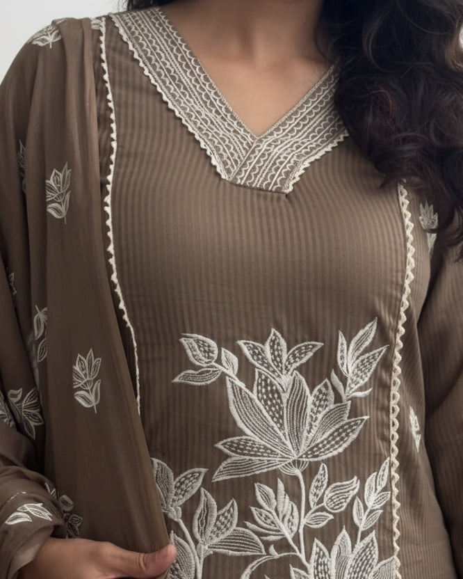 Person wearing a brown dress with white floral embroidery and matching brown dupatta.