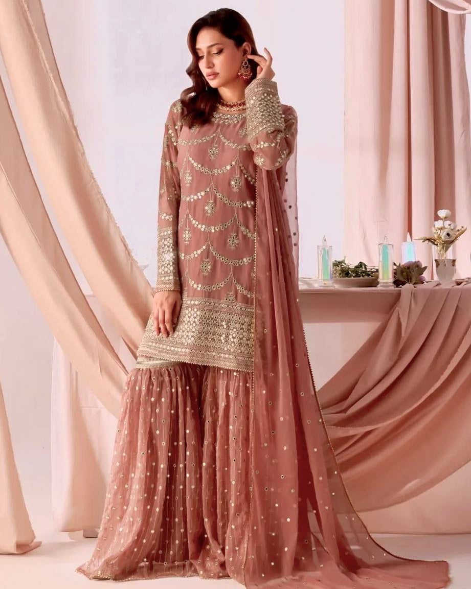 Woman in a traditional pink and gold outfit standing in front of draped curtains.