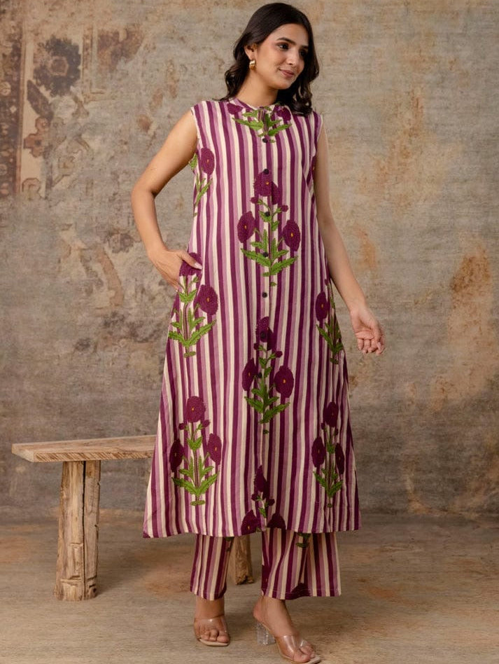 Woman wearing a sleeveless dress with floral patterns against a textured wall.