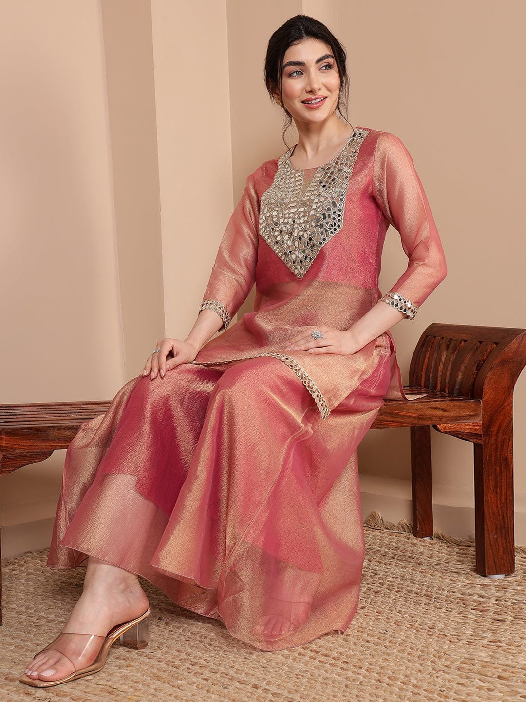 Woman wearing a pink saree with silver embroidery sitting on a wooden bench.