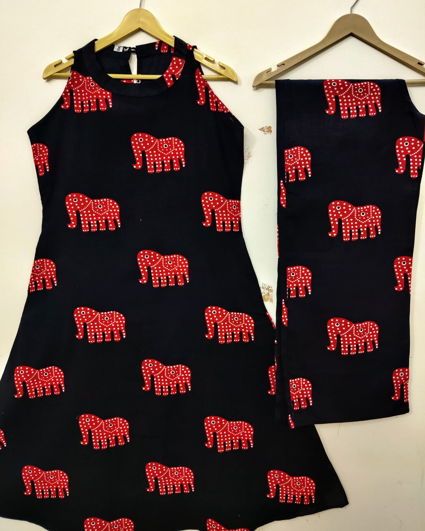 Black sleeveless top and skirt set with red elephant patterns on hangers.