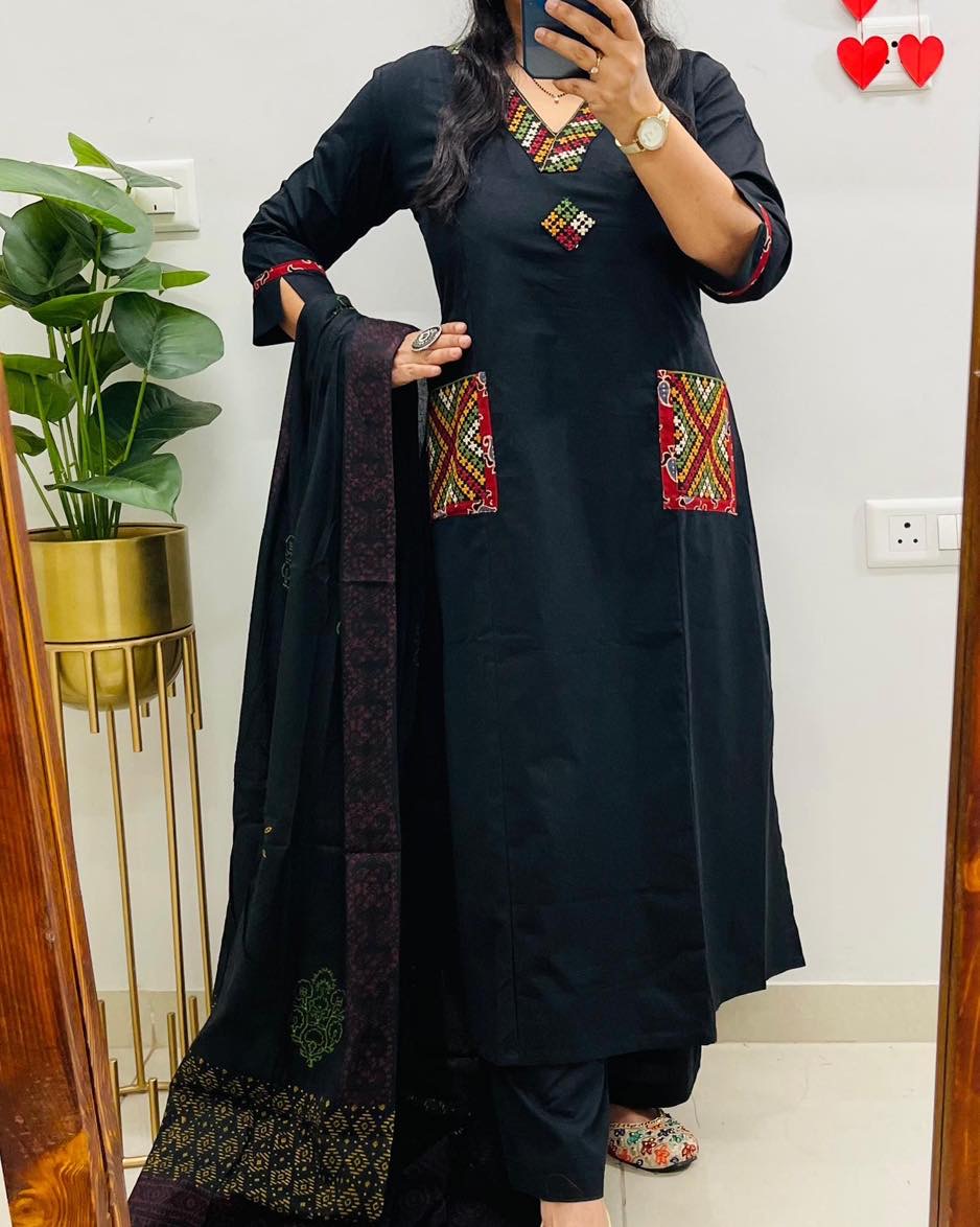 Person wearing a black traditional outfit with colorful embroidery, standing indoors.