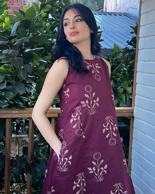 Woman wearing a purple dress with floral patterns standing outdoors.