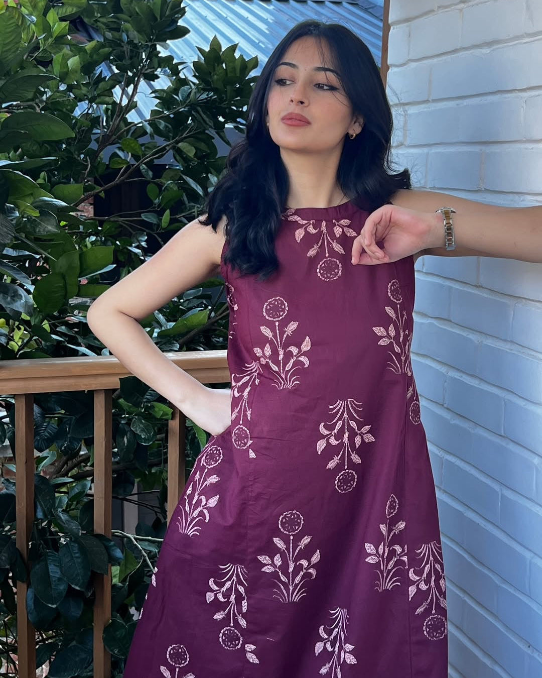 Woman wearing a purple dress with floral patterns standing outdoors.