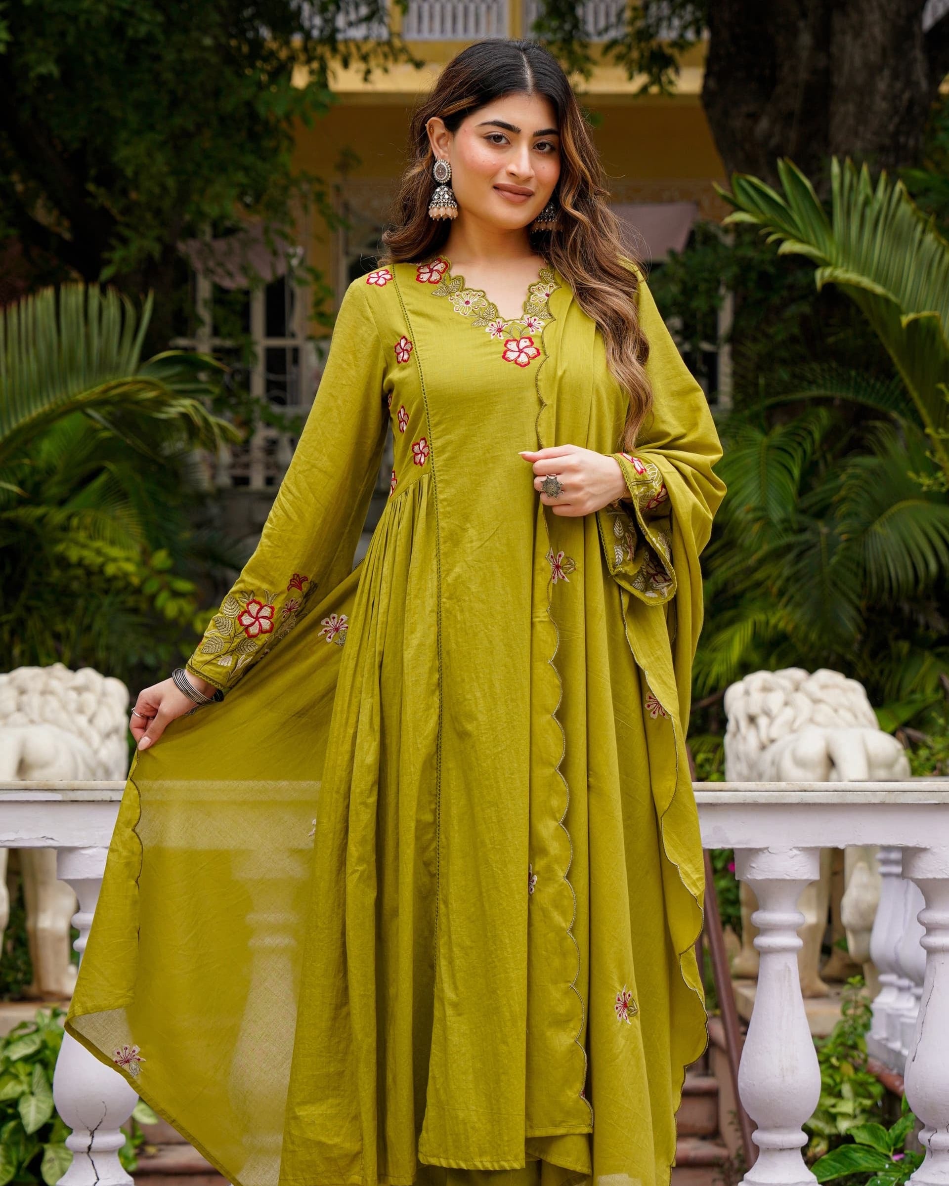 Woman in a green traditional outfit standing outdoors with greenery in the background
