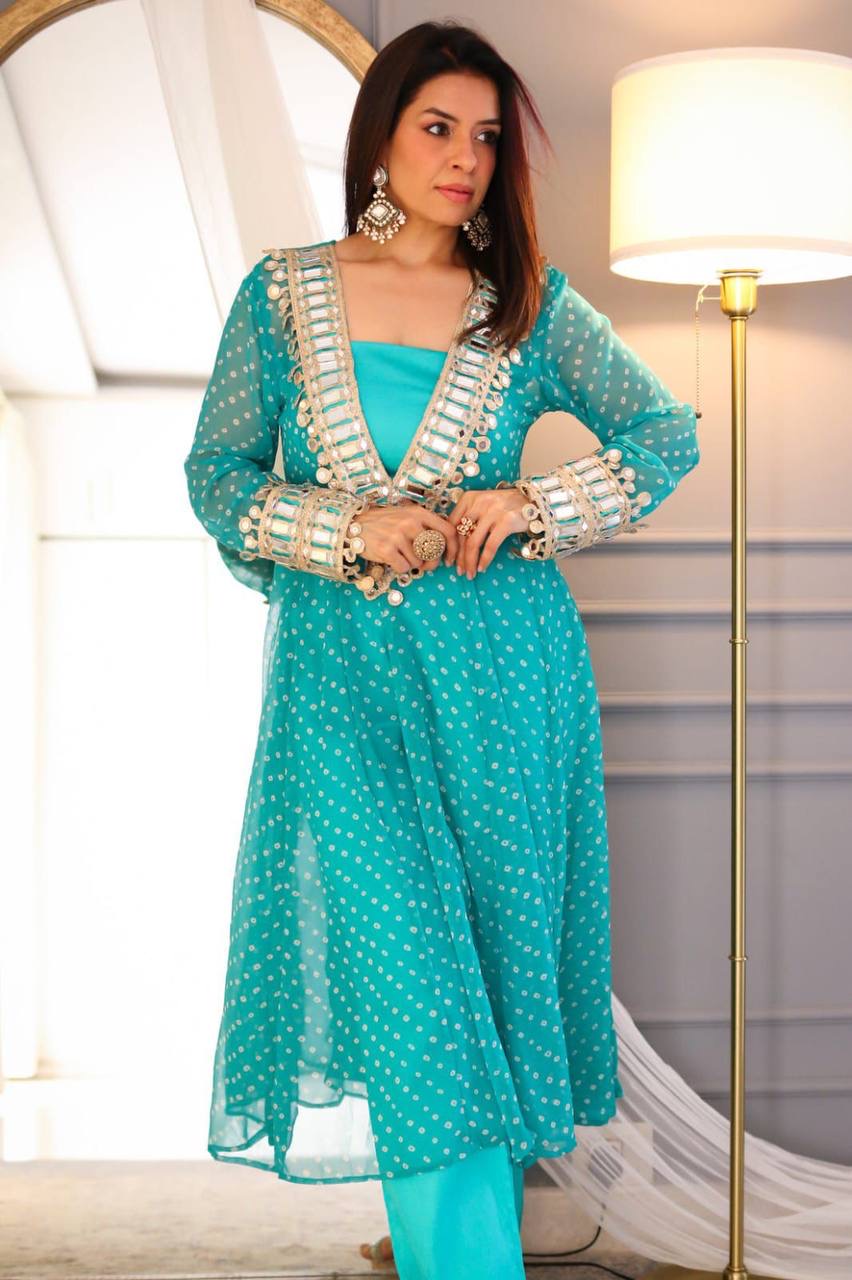 Woman wearing a turquoise traditional outfit with white patterns in a well-lit room.