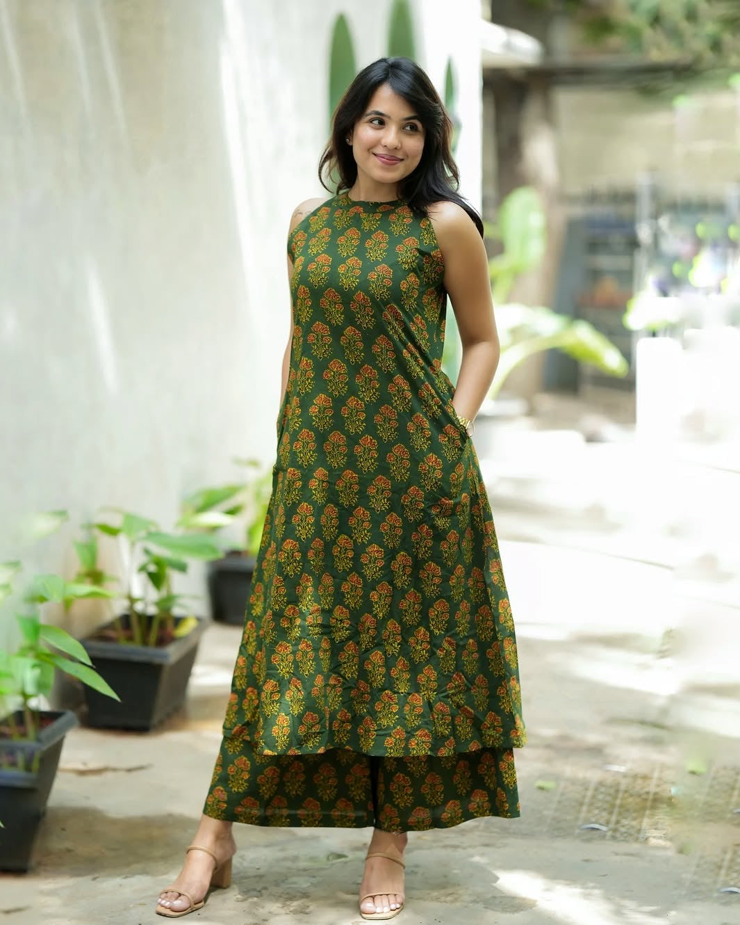Woman wearing a green patterned dress standing outdoors with plants in the background