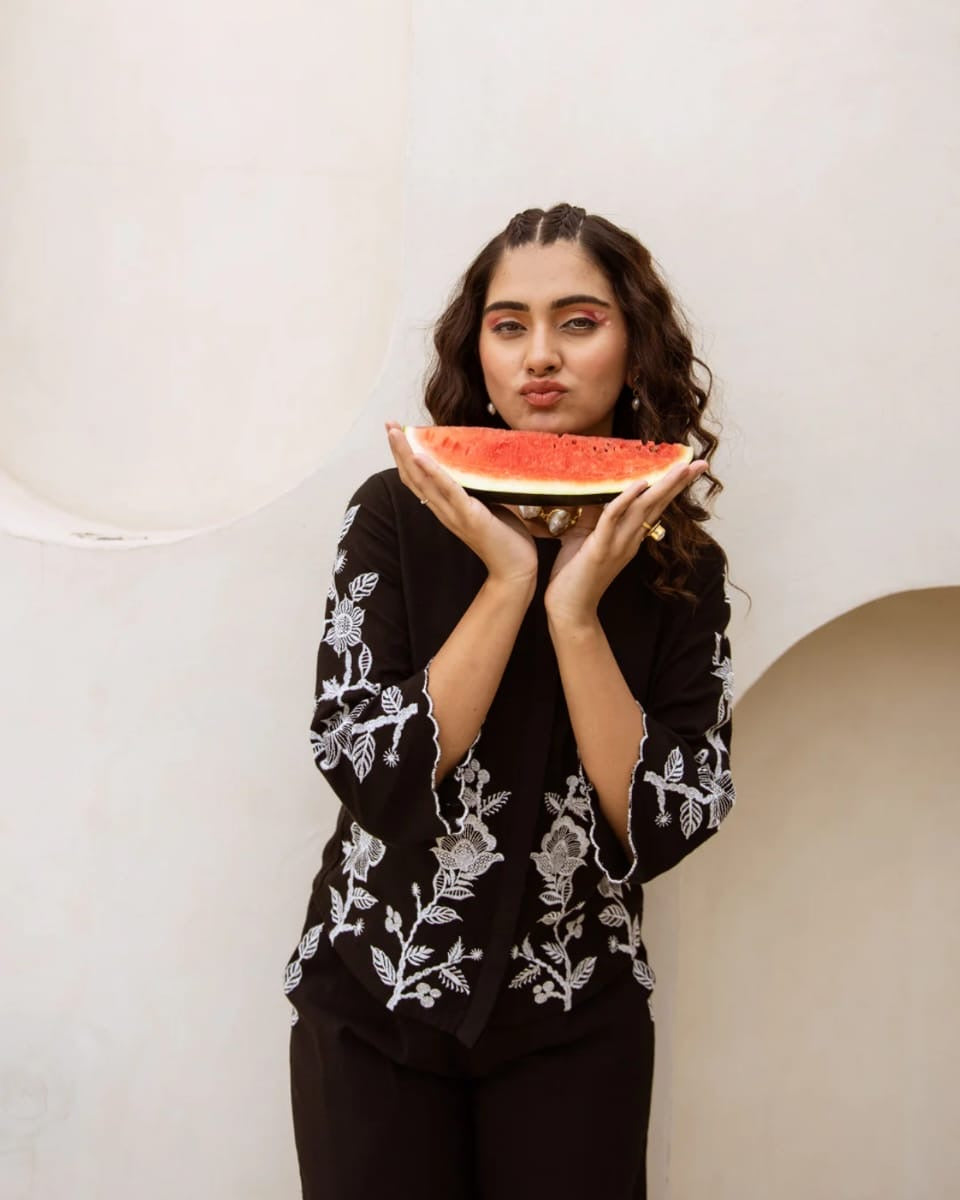 Person holding a slice of watermelon in front of their face against a plain background