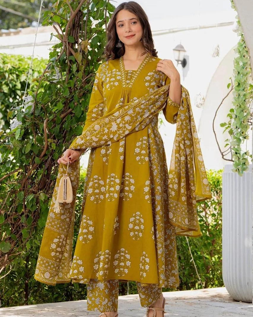 Woman in a yellow floral outfit standing outdoors with greenery in the background