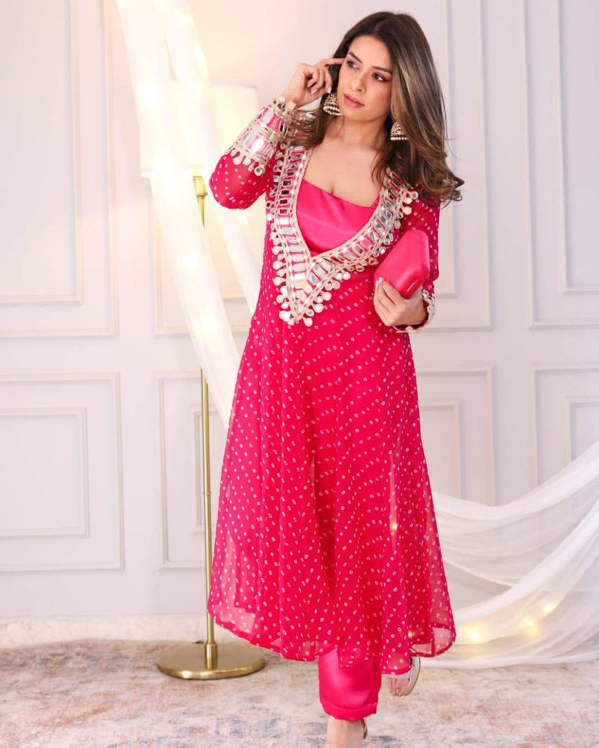 Woman in a pink traditional outfit with white patterns against a white wall.