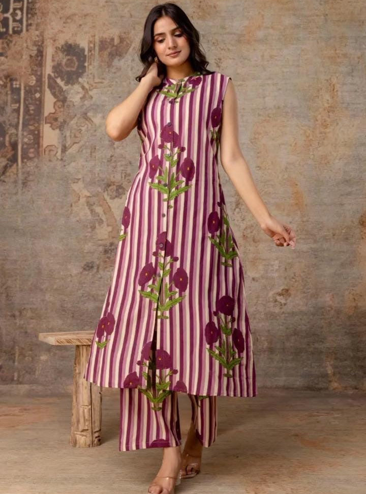 Woman wearing a pink and purple striped dress with floral patterns against a textured wall.