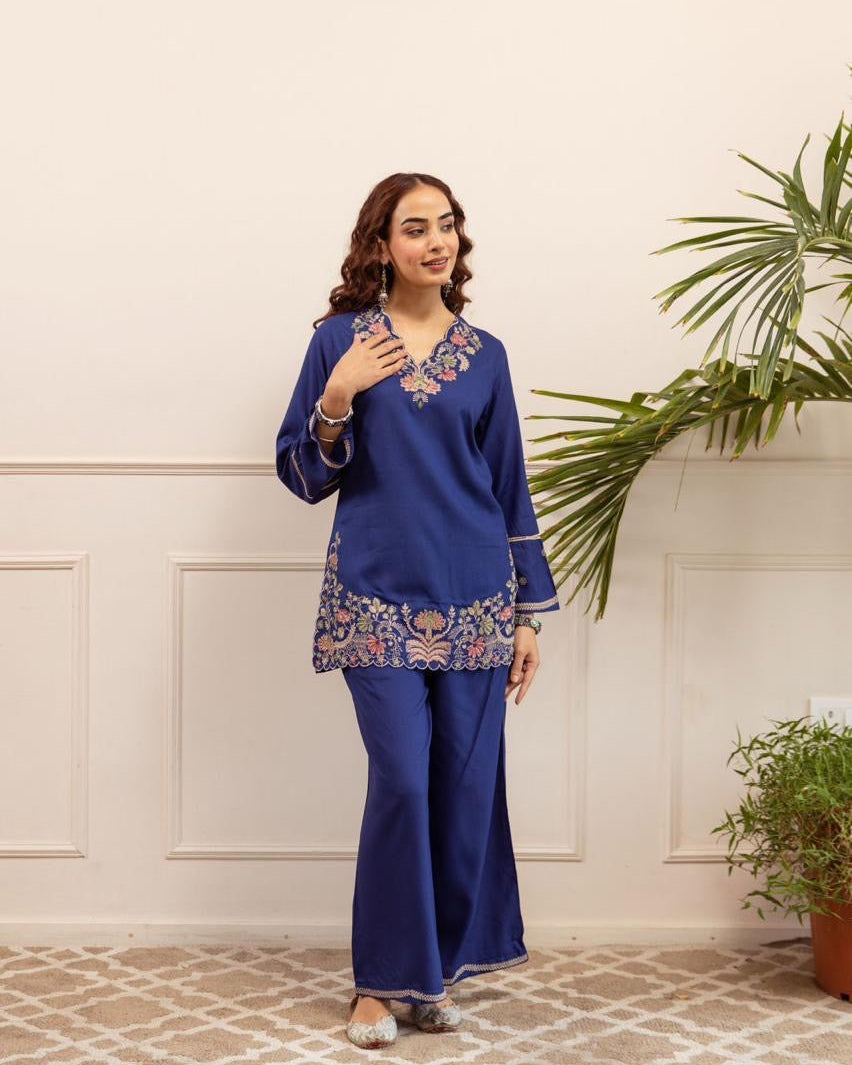 Woman wearing a blue traditional outfit with floral patterns in a room with plants.
