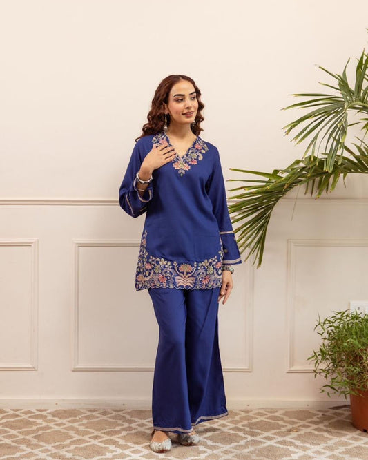 Woman wearing a blue traditional outfit with floral patterns in a room with plants.