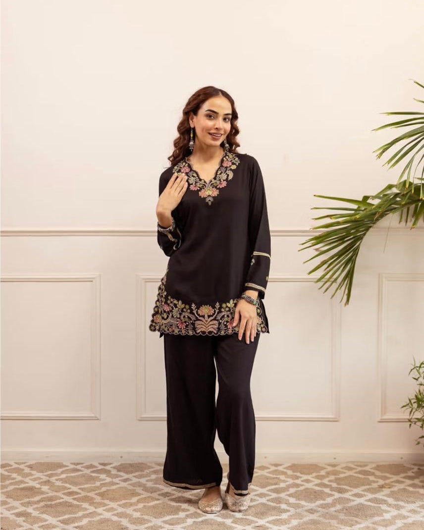 Woman wearing a black outfit with floral embroidery in a room with a white wall and patterned floor.