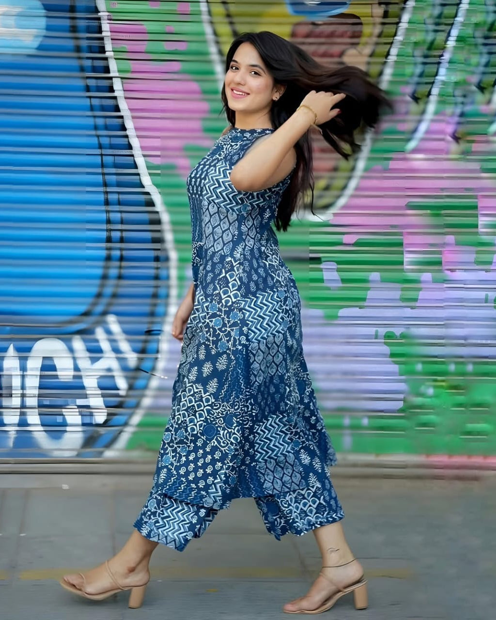 Woman in a blue patterned dress standing in front of a colorful graffiti wall.