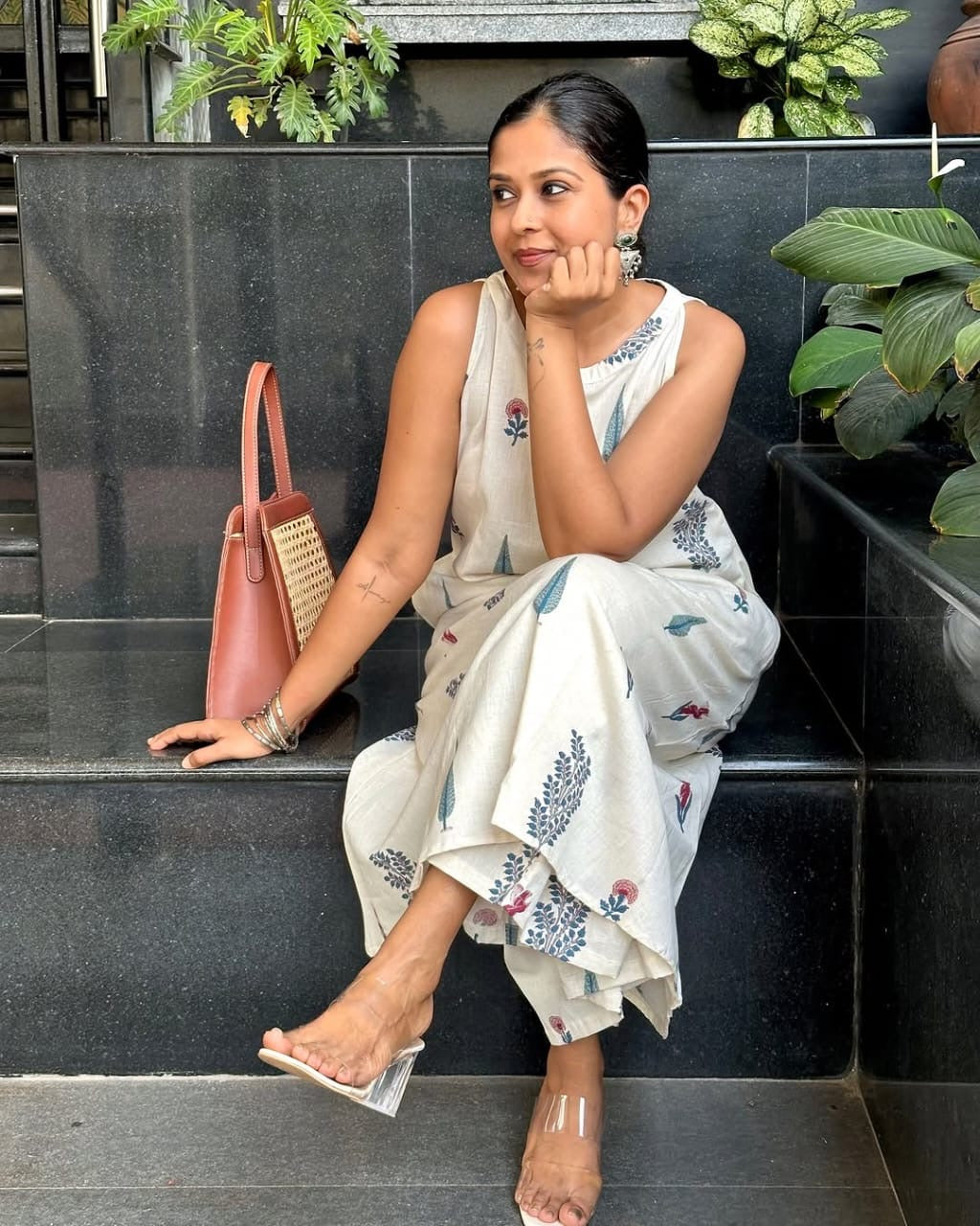 Woman in a floral saree sitting on steps with a pink handbag.