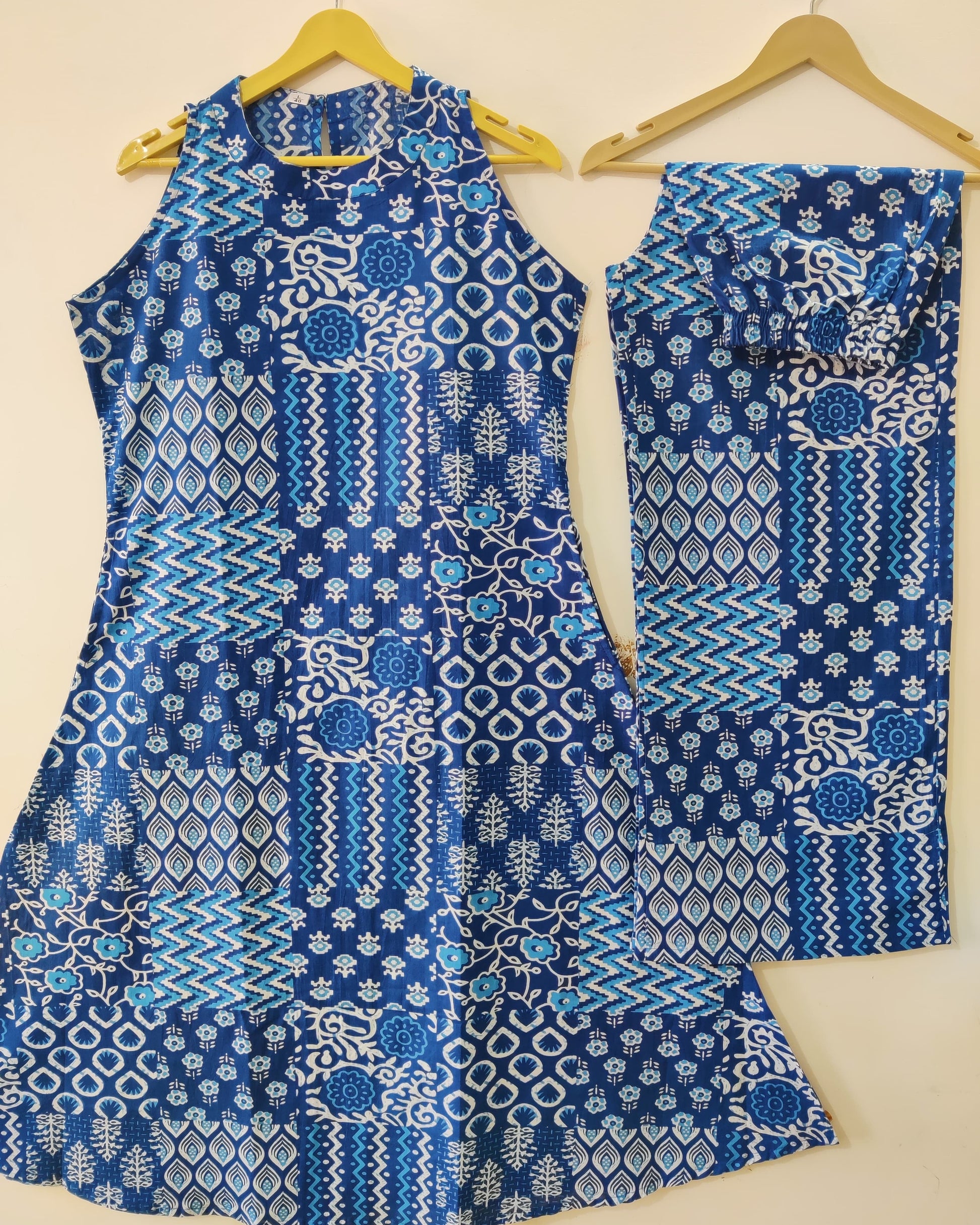 Blue and white patterned sleeveless top and pants on hangers against a beige background
