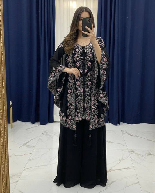 Person wearing a floral dress and black pants in front of a mirror with blue curtains.