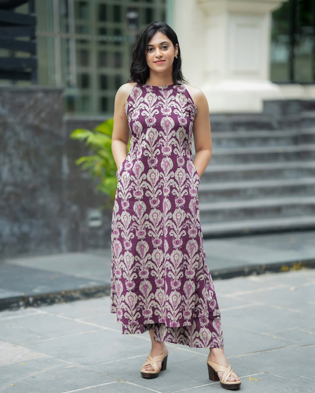 Woman wearing a purple floral dress standing outdoors on a stone path.