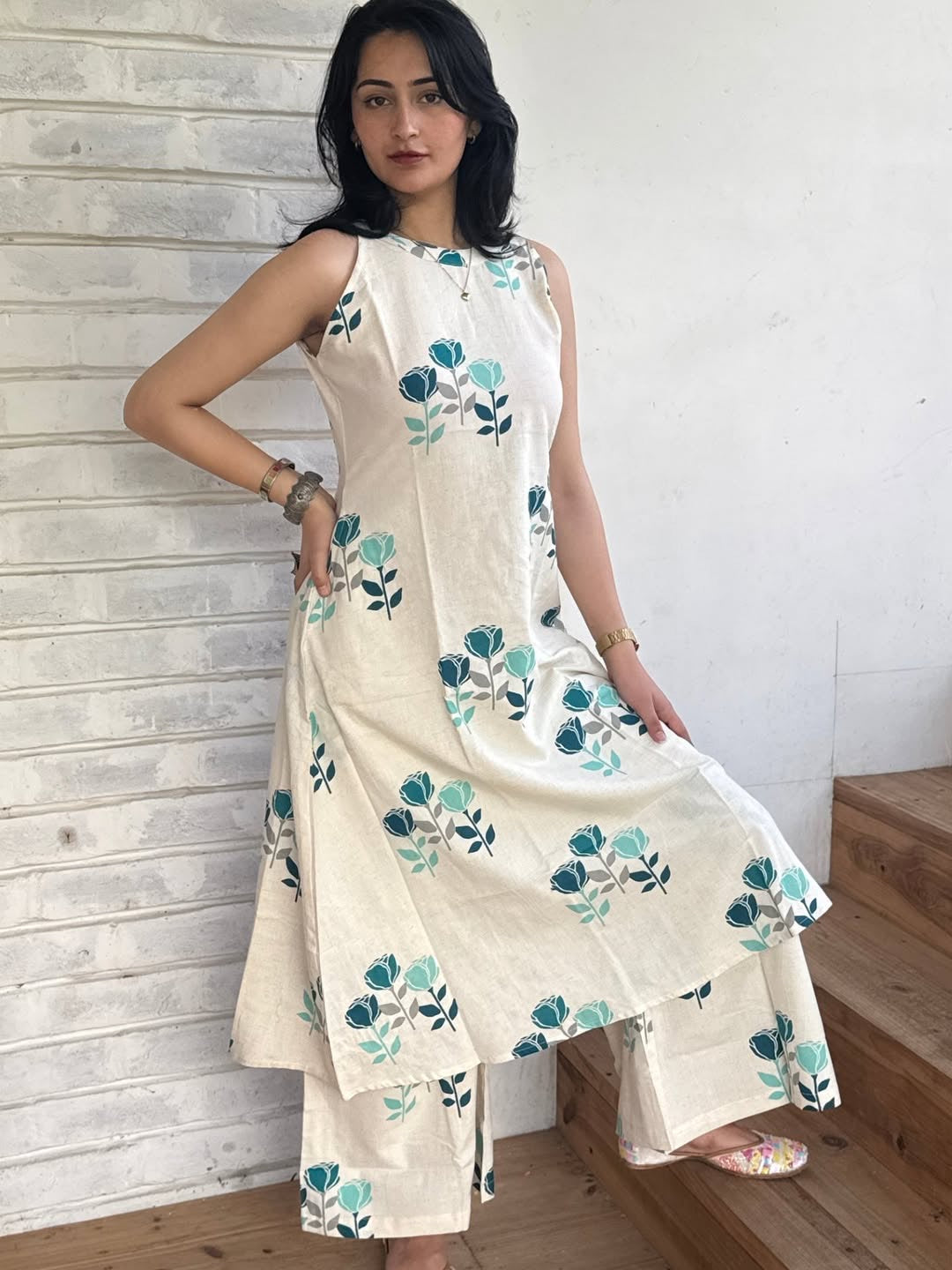 Woman wearing a floral dress standing against a white wall.