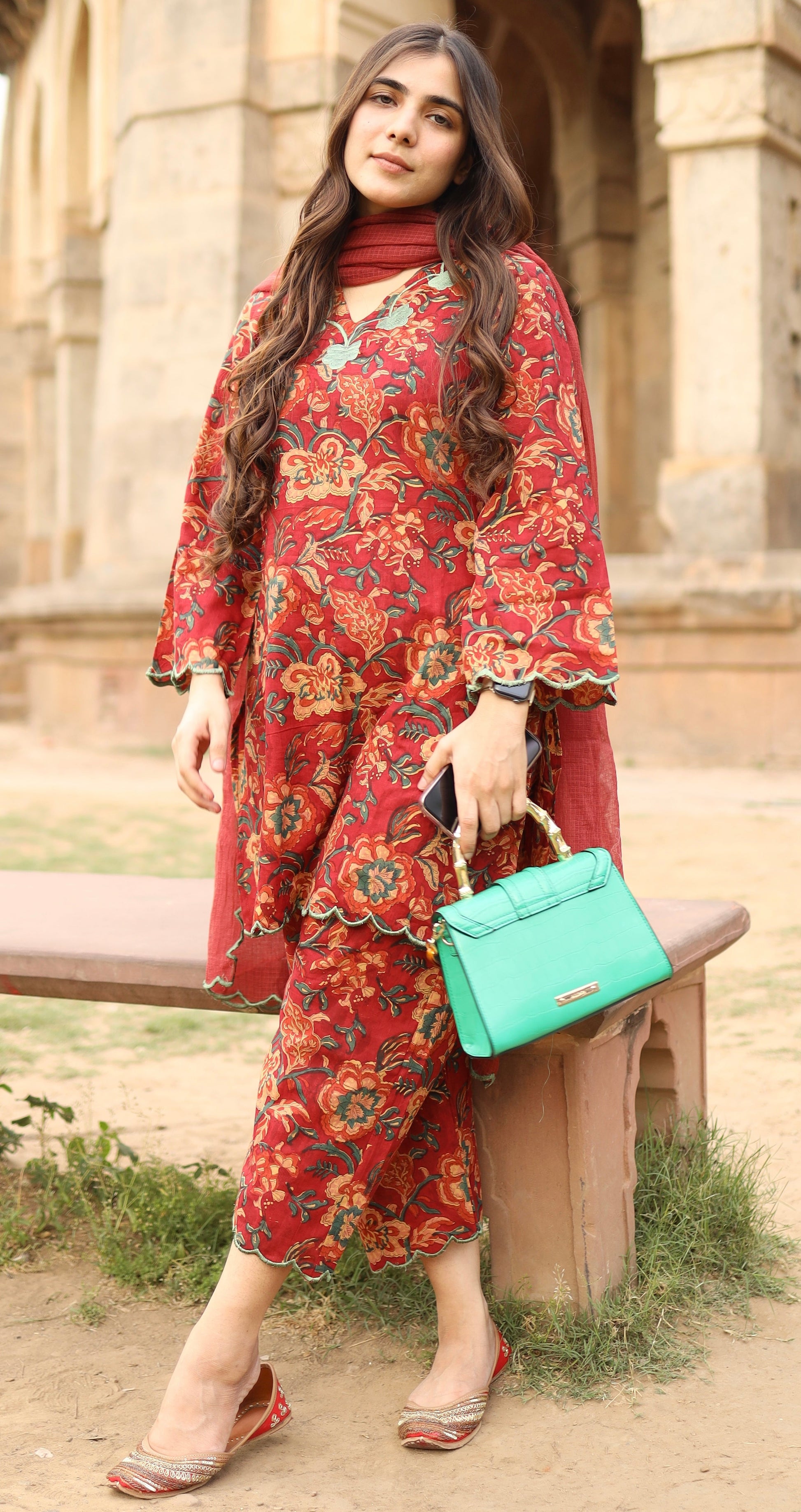 Woman in a red floral dress holding a green handbag outdoors.