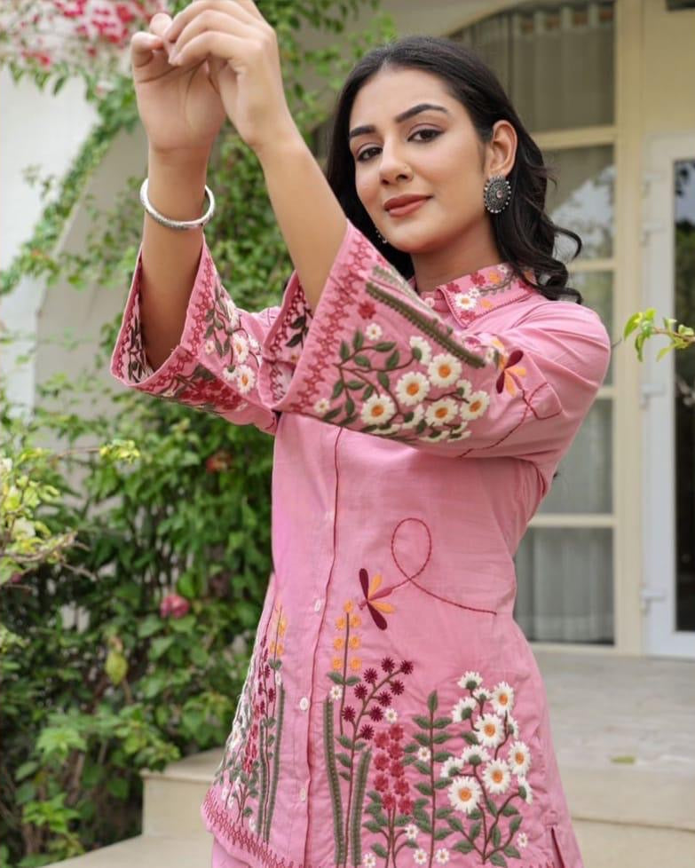 Woman wearing a pink embroidered dress outdoors with greenery in the background