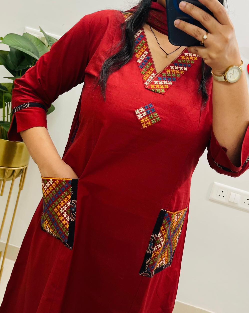 Person wearing a red traditional outfit with colorful embroidery, taking a mirror selfie.