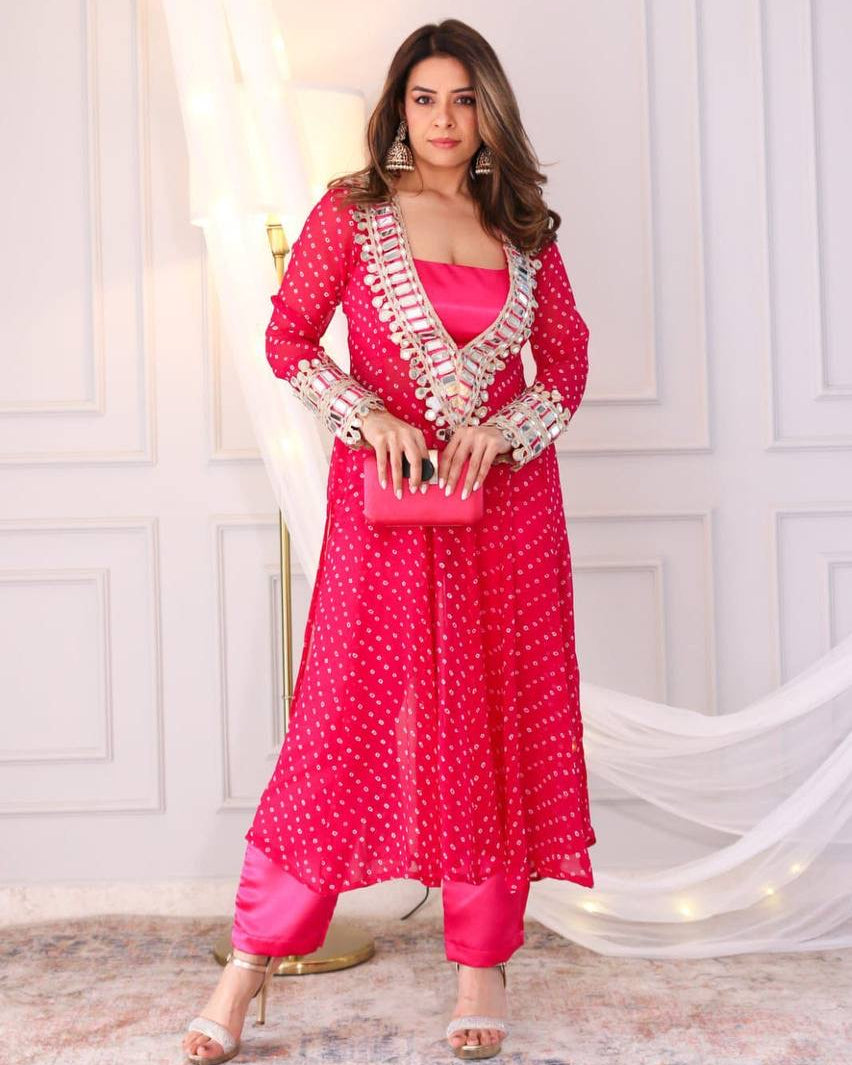 Woman in a bright pink traditional outfit with white patterns standing against a white wall.