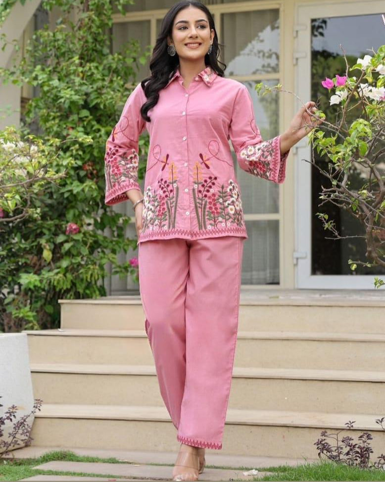 Woman in a pink traditional outfit standing outdoors with greenery in the background
